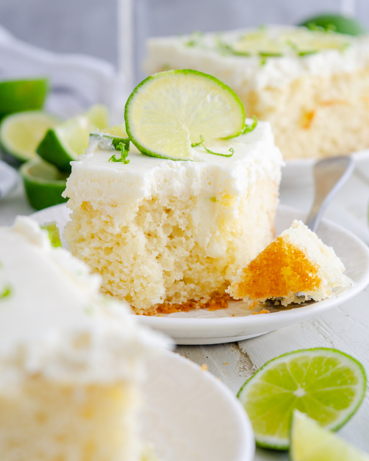 Key lime poke cake food photography on a white plate with a bite out of it.
