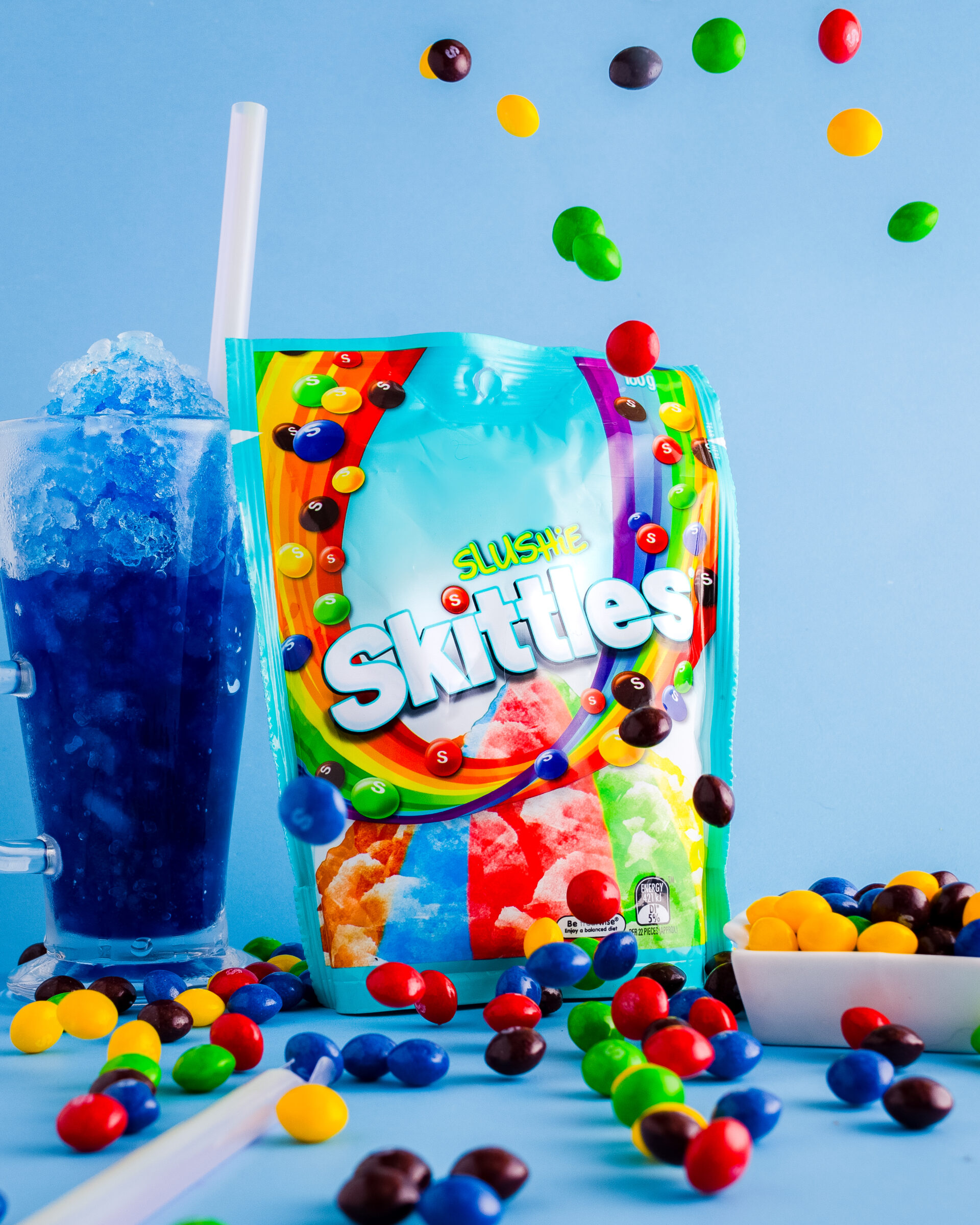 Slushie skittles package with skittles raining down, and blue slushie in the background.