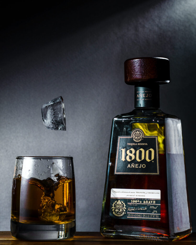 Tequila bottle and a glass with ice dropping in - professional product photography